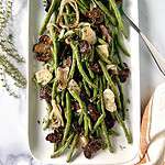 Roasted mushrooms, shallots and green beans on a rectangular platter with a metal serving spoon.