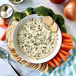 Vegan onion dip in a bowl surrounded by broccoli florets, baby carrots and vegan crackers.