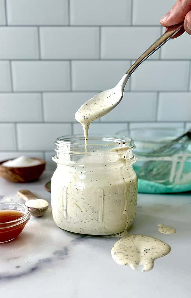 Whole30 ranch dressing in a jar with a spoon over it pouring more dressing into the jar.