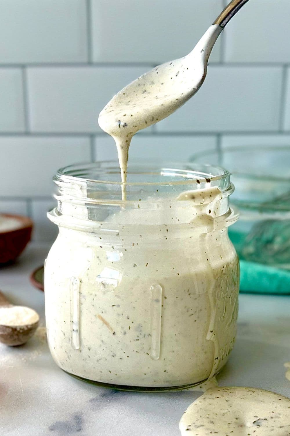 Dairy free ranch dressing in a mason jar with a spoon pouring more dressing into the jar.