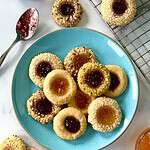 Dairy-free thumbprint cookies piled on a plate next to a cooling rack with more cookies on it.