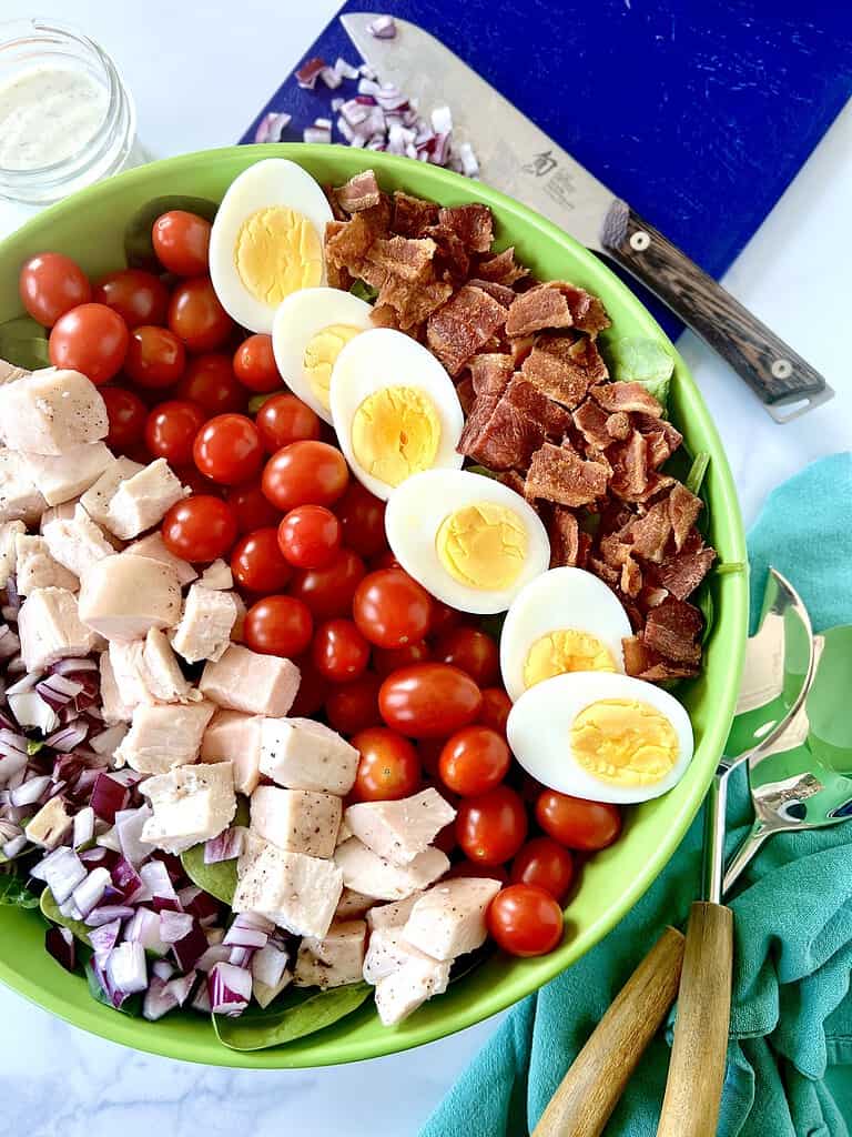 Low carb cobb salad in a large bowl with diced red onion, chicken, grape tomatoes, hard boiled eggs and chopped bacon.