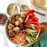 A salmon poke bowl with salmon chunks, sugar snap peas, red bell pepper strips and shredded carrots.