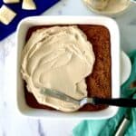 Paleo banana cake in a square baking dish with some cream cheese frosting spread over part of it.