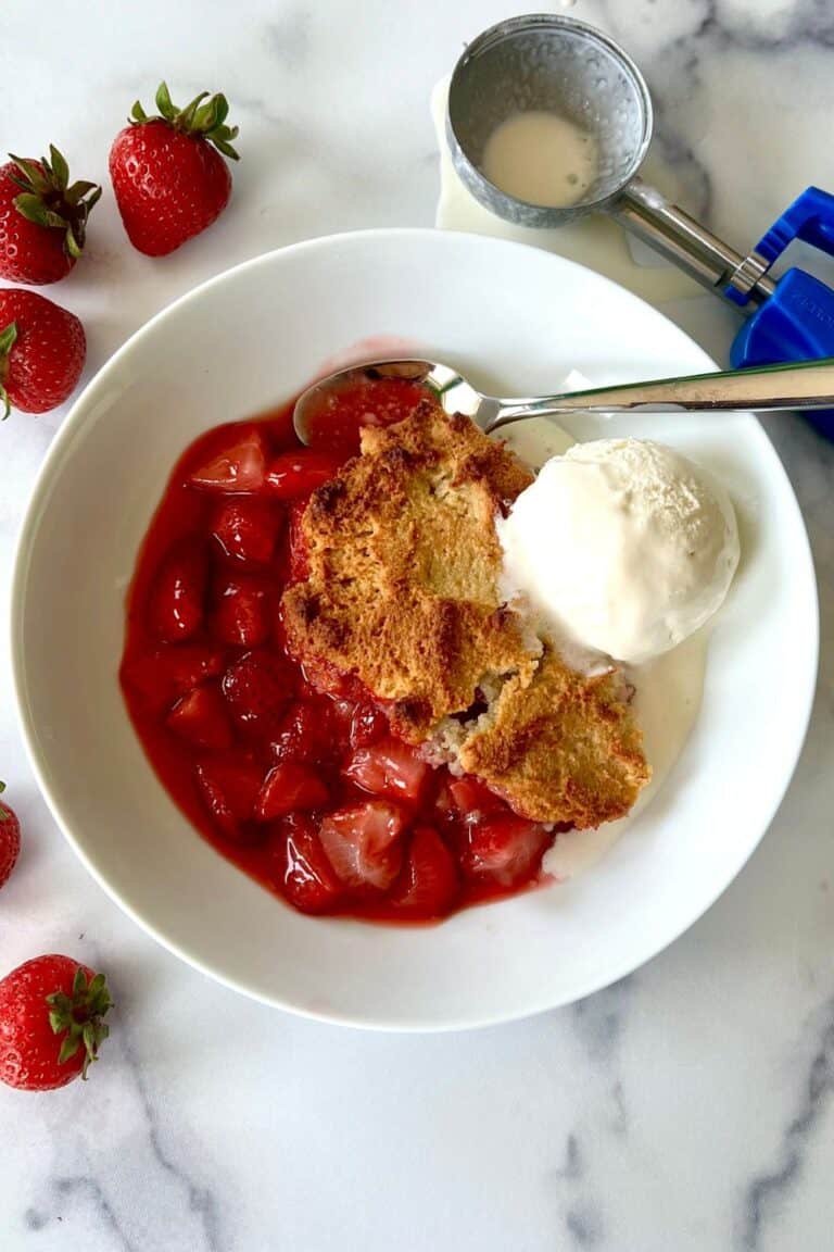 Paleo strawberry cobbler in a bowl with a scoop of vanilla ice cream and a spoon.