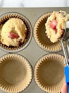 Scooping strawberry muffin batter into a muffin pan.