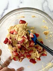 Stirring strawberry muffin batter with a spatula in a glass bowl.
