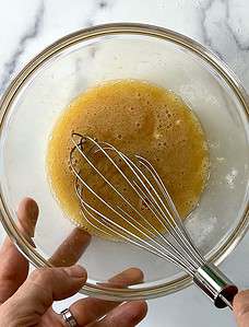 Whisking wet muffin ingredients in a glass bowl.