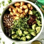 The ingredients for an avocado peach salad arranged in piles in a big bowl.
