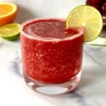 A frozen cherry mocktail with orange juice in a glass with a lime slice on the rim.