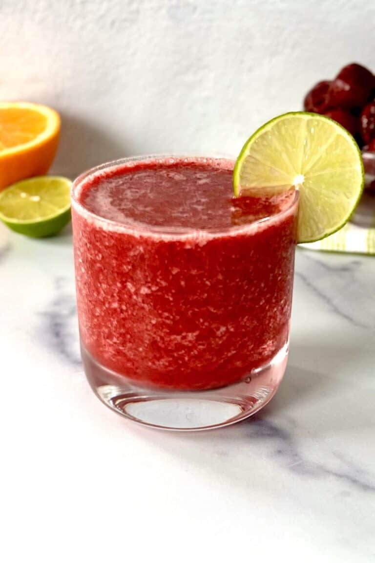 A frozen cherry mocktail with orange juice in a glass with a lime slice on the rim.