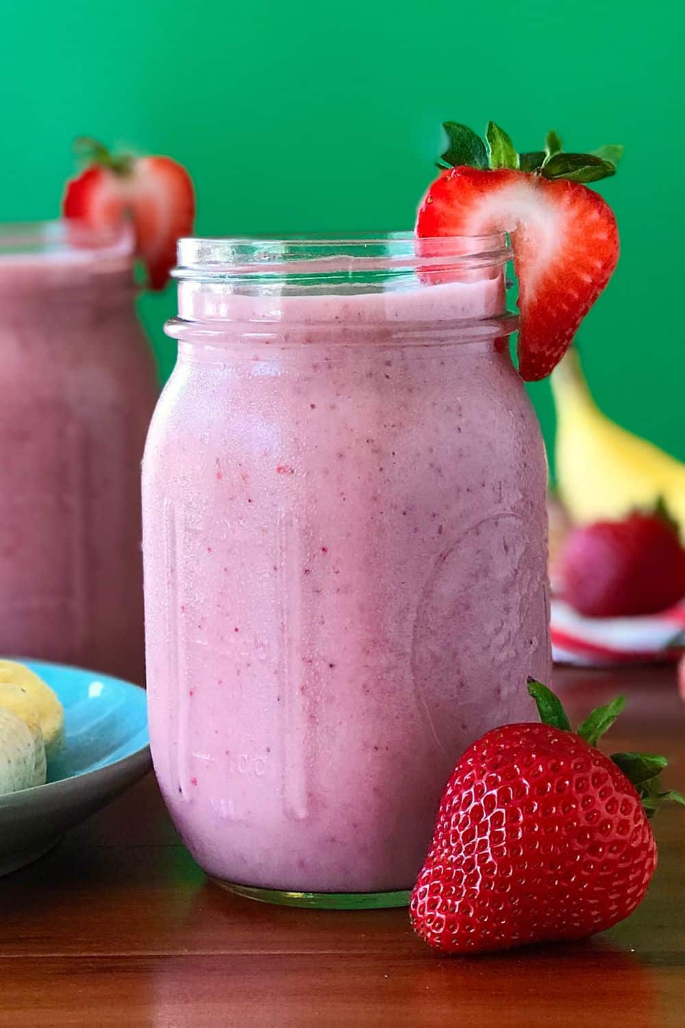 A banana strawberry smoothie in a mason jar with a strawberry slice on the rim.