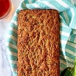 A loaf of gluten-free zucchini bread on a striped towel next to 2 zucchini.