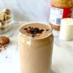 A chocolate peanut butter smoothie in a tall glass drizzled with peanut butter and topped with bits of chocolate.