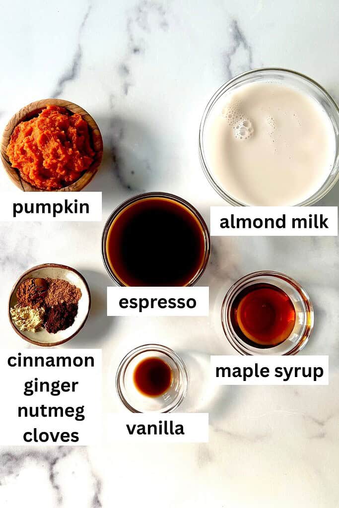 All the ingredients for a paleo pumpkin spice latte in individual bowls on a marble surface.