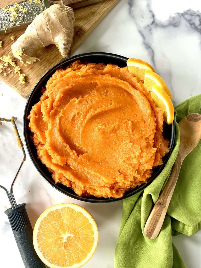 Vegan mashed sweet potatoes with ginger and orange in a bowl garnished with orange slices.