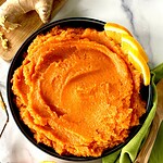 Mashed sweet potatoes with ginger and orange in a bowl garnished with orange slices.